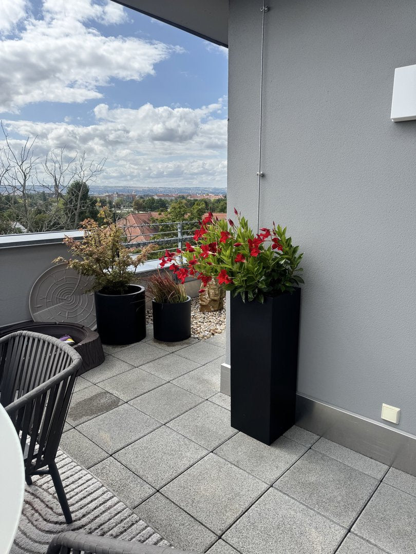 Pflanzkübel Fiberglas Säule 30x30x90cm elegant schwarz matt mit roter Blütenbepflanzung auf einer Dachterrasse