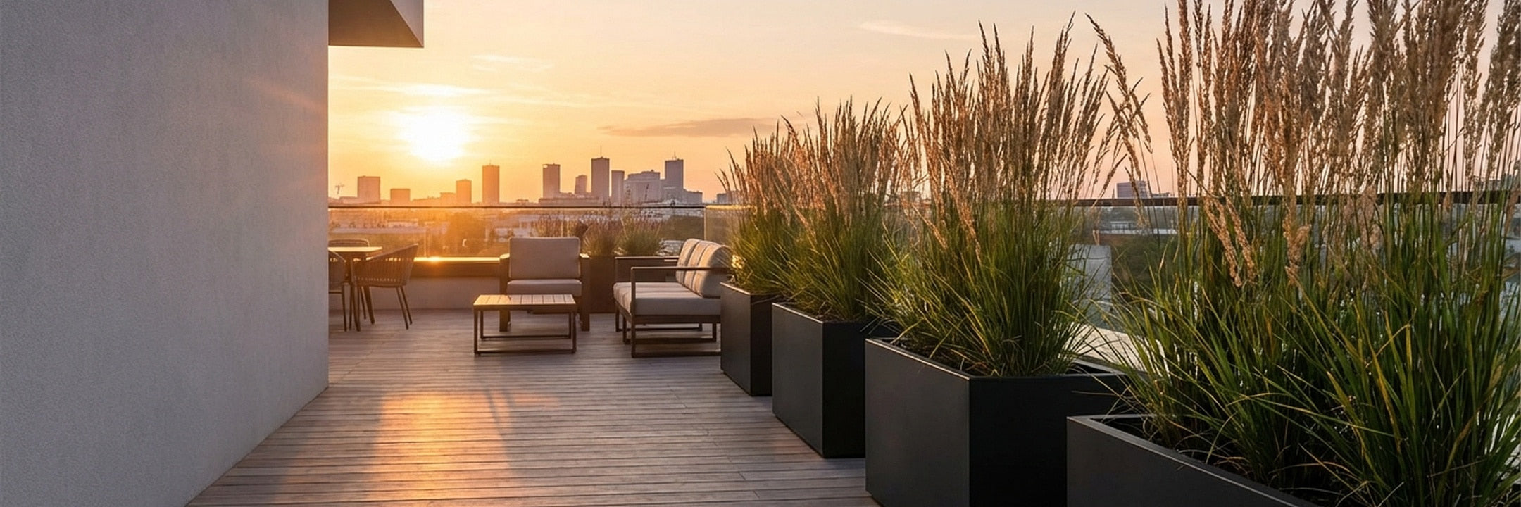 Moderne Dachterrasse mit langen schwarzen Pflanztrögen und Gräsern bei Sonnenuntergang – elegante rechteckige Pflanzkübel für die Stadtwohnung.